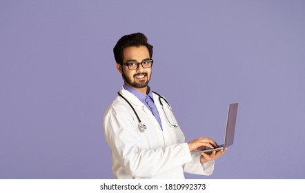 Cyber Medicine Concept. Happy Indian Doctor Talking To Patient Online On Laptop Computer, Violet Background. Panorama