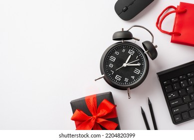 Cyber monday concept. Top view photo of giftbox with ribbon bow alarm clock computer mouse keyboard pencils and red paper bag on isolated white background with copyspace