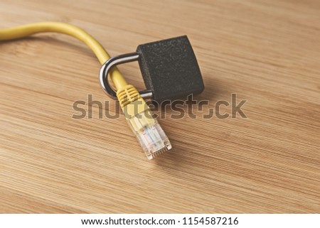 A cyber security concept image consisting of an Ethernet cable, padlock and a wooden background.  