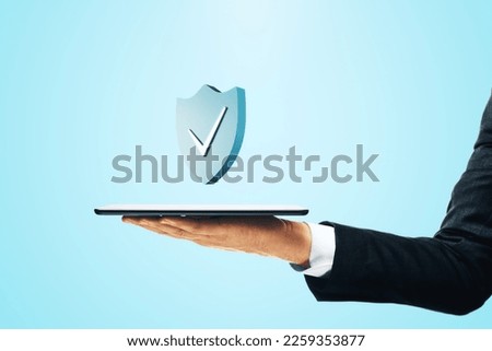 Cyber security and network protection concept with check mark on blue shield above digital tablet in businessman hand on abstract light background