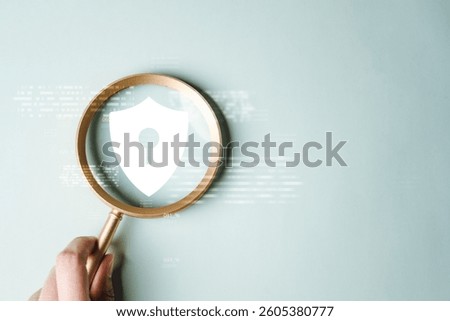 Cyber security system technology. Secure information privacy. Crime network technology. A person is holding a magnifying glass over a white shield with a keyhole. The shield is a symbol of protection.