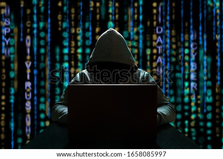 Cyber threat of an unknown hacker sitting in front of a computer against a background of binary code. Cyber security
