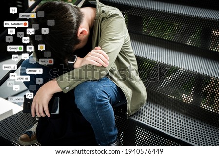 Cyberbullying - social media harassment concept. An asian preteen, teenager boy sitting alone hold a smartphone feeling frustrated after reading bad comments. Text emoticons, Teen mental health.