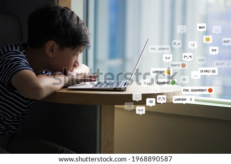 Cyberbullying - social media harassment concept. Portrait of a boy sitting alone staring at notebook computer screen feeling frustrated while reading bad comments. Text emoticons, Kids mental health.