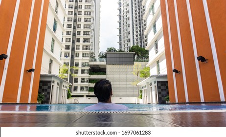 Cyberjaya, Malaysia - March 1, 2020: Back View Portrait Of Young Malay Man Leaning At The Side Of The Swimming Pool Looking At The Tall Building In The City. Luxury Lifestyle Concept. 