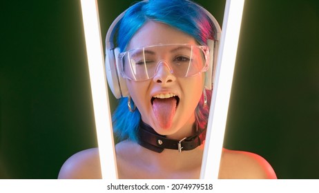 Cyberpunk model. Party girl. Futuristic generation. Funky attractive playful woman sticking tongue out in LED neon light isolated on dark background.