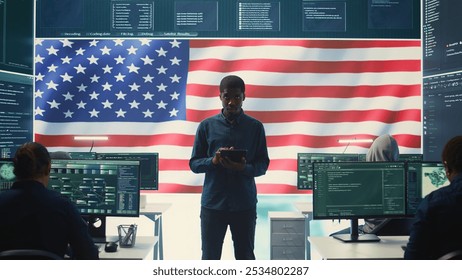 Cybersecurity expert working in a governmental hacking room with the American flag shown on big screen. Safeguarding data protection and doing cyber threat analysis in a high tech office. Camera B.