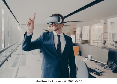 Cyberspace experience at work. Happy man office worker wearing vr goggles, pointing with finger at objects in digital world, businessman in 3d glasses interacting with virtual reality, dressed in suit - Powered by Shutterstock