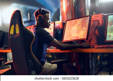 Cybersport concept. Side view of a focused african guy, professional gamer wearing headphones participating in eSport tournament
