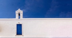 Cyclades, Greece. Small White Church Wall And Belfry Against Blue Sky, Sunny Day. Copy Space