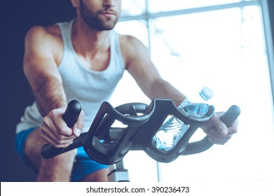 Cycling At Gym. Part Of Low Angle View Of Young Man In Sportswear Cycling At Gym