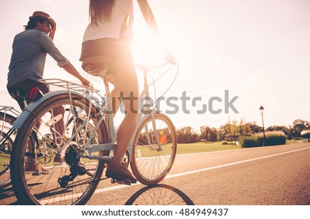 Cycling together. Low angle view of young people riding bicycles along a road together