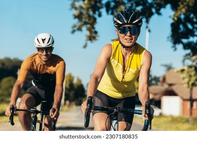 Cycling woman and man riding on bikes outside of the city. Outdoor sport activity. Young smiling couple cycling. Healthy lifestyle. Focus on a woman in the front wearing sunglasses and a helmet. - Powered by Shutterstock