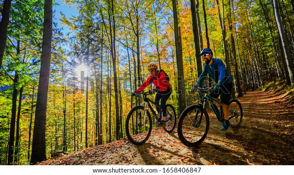 Cycling woman and man riding on bikes at sunset\
mountains forest landscape. Couple cycling MTB enduro flow trail\
track. Outdoor sport\
activity.