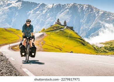 Cyclist back view on the road in scenic caucasus nature with Gergeti trinity monastery in the background. Traveller on bicycle. Solo travel long distance bicycle touring concept