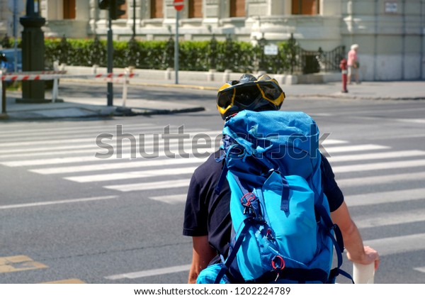 Cyclist in the city with a blue backpack with\
a protective helmet stands near the light traffic light, the theme\
of cycling and city\
transport\
