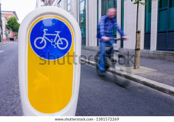 A cyclist cycles past a bollard dividing a cycle\
lane from the main road.