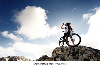 Cyclist Drinks Water On Top Of A Mountain With Bike On A Sunny Day