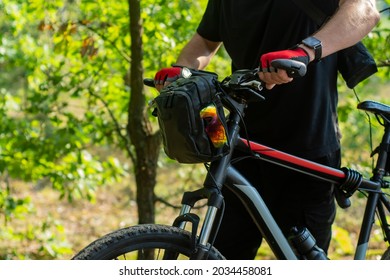 A cyclist in gloves near a mountain bike with a bag on the handlebars