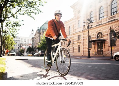 A cyclist in a helmet goes to work with a briefcase. Urban ecotransport.  Fitness watch on hand. - Shutterstock ID 2204197803