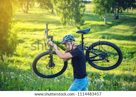 Cyclist man in helmet carries his mountain bike in the rise in the background green nature. Concept of active and healthy lifestyle