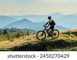 Cyclist man riding electric bike outdoors on sunny day. Male tourist resting on grassy hill, enjoying beautiful mountain landscape, wearing helmet and backpack. Concept of active leisure.