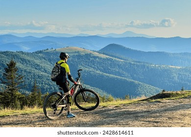 Cyclist man riding electric bike outdoors on sunny day. Male tourist resting on hill, enjoying beautiful mountain landscape, wearing helmet and backpack. Concept of active leisure. - Powered by Shutterstock