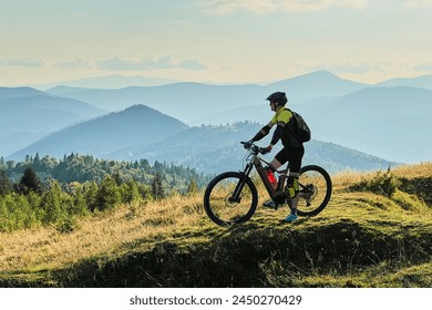 Cyclist man riding electric bike outdoors on sunny day. Male tourist resting on grassy hill, enjoying beautiful mountain landscape, wearing helmet and backpack. Concept of active leisure. - Powered by Shutterstock