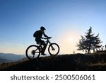 Cyclist man riding electric mountain bike outdoors. Male tourist biking along grassy trail in the mountains, wearing helmet and backpack. Concept of sport, active leisure and nature.