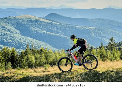 Cyclist man riding electric mountain bike outdoors. Male tourist biking along grassy trail in the mountains, wearing helmet and backpack. Concept of sport, active leisure and nature. - Powered by Shutterstock