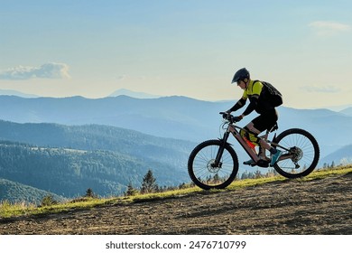 Cyclist man riding electric mountain bike outdoors. Male tourist biking along grassy trail in the mountains, wearing helmet and backpack. Concept of sport, active leisure and nature. - Powered by Shutterstock