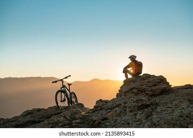Cyclist mtb biker sits and relax on mountain top at sunset
