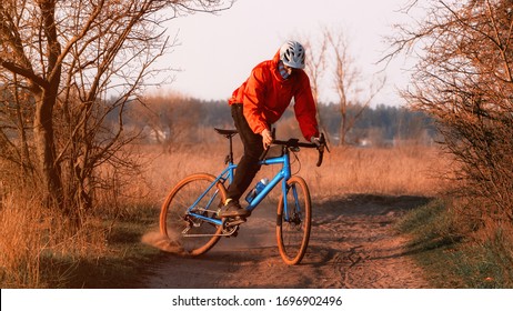 A cyclist on a gravel bike rides along the road raising dust from the rear wheel at sunset. Gravel biking. Extreme sports and activity concept. - Shutterstock ID 1696902496
