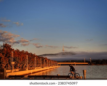 Cyclist on lake burley griffin in autumn with black mountain tower in the distance