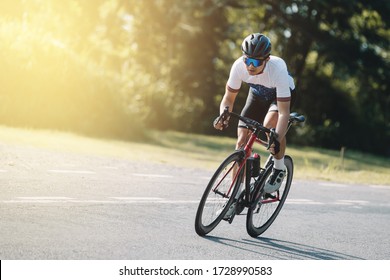Велосипедист крутит педали на гоночном велосипеде на открытом воздухе на закате. Изображение велосипедиста в движении на заднем плане вечером.