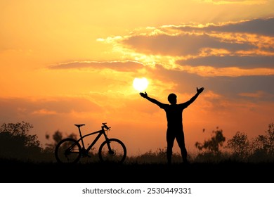 A cyclist raises arms in triumph beside a bicycle, silhouetted against a stunning sunset sky, symbolizing freedom and adventure. - Powered by Shutterstock