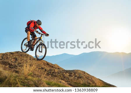 Cyclist in Red Jacket Riding the Bike in the Beautiful Mountains Down the Rock on the Sunrise Sky Background. Extreme Sport and Enduro Biking Concept.