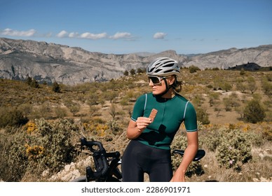 Cyclist is resting.Female cyclist is wearing cycling kit holding energy snack for endurance during bicycle training.Sport nutrition.Sport snack for cyclist.Granola energy bar. - Powered by Shutterstock