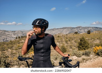 Cyclist is resting.Male cyclist is wearing cycling kit holding energy snack for endurance during bicycle training.Sport nutrition.Sport snack for cyclist.Granola energy bar. - Powered by Shutterstock