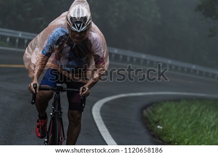 The cyclist ride his bicycle up high on hill, Cycling to destination no matter how bad weather is. Foggy, windy, raining and cold day. Focus on cyclist's face.