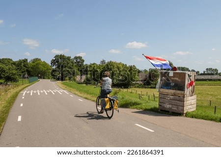 A cyclist rides on a dike in the Betuwe past a stall with cherries.