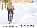 Cyclist rides on snow and snowdrifts in city during blizzard. Man in warm clothes wearing protective helmet riding on snowy slippery road on bicycle. Risk of cycling in winter. Winter cycling hazard