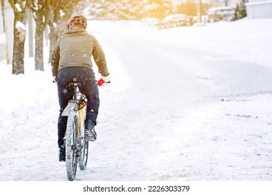 Cyclist rides on snow and snowdrifts in city during blizzard. Man in warm clothes wearing protective helmet riding on snowy slippery road on bicycle. Risk of cycling in winter. Winter cycling hazard - Powered by Shutterstock