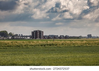 Cyclist riding along an elevated path through a Dutch polder landscape with the skyline of a new residential area in the background.