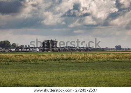 Cyclist riding along an elevated path through a Dutch polder landscape with the skyline of a new residential area in the background.