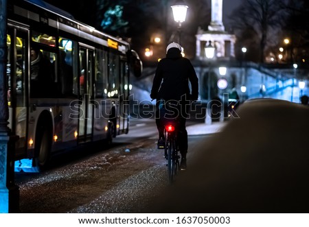 A cyclist riding alongside the bus in the illuminated city at night