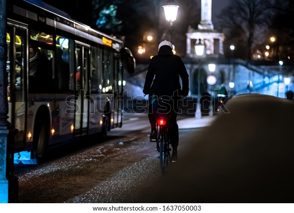 A cyclist riding alongside the bus in the\
illuminated city at night