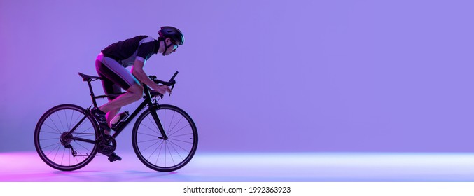Cyclist riding a bicycle isolated on studio background in gradient lilac pink neon light. Concept of active life, rest, travel, energy, sport