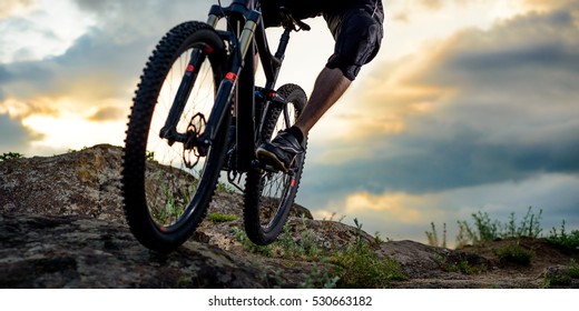 Cyclist Riding the Bike Down Rocky Hill at Sunset. Close up Extreme Sport Concept. Space for Text.