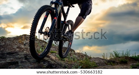 Cyclist Riding the Bike Down Rocky Hill at Sunset. Close up Extreme Sport Concept. Space for Text.